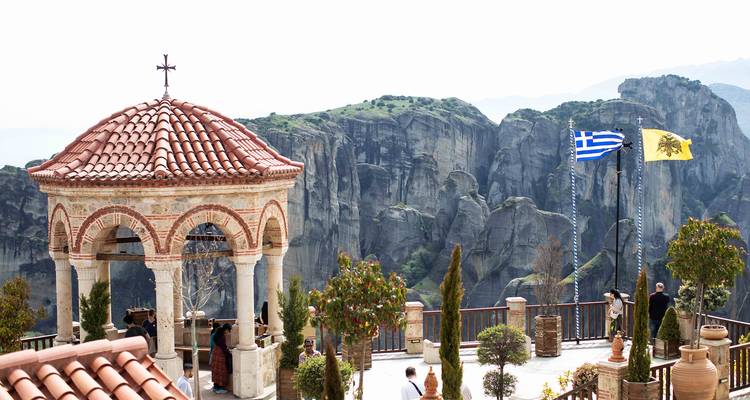 Terras van een klooster in Meteora met Griekse en Byzantijnse vlaggen met uitzicht op dramatische rotsformaties.