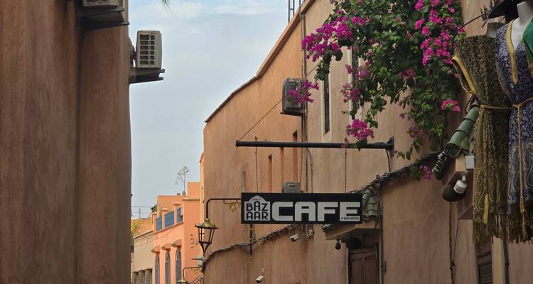 Callejón estrecho de la medina con un cartel de Bazaar Cafe y buganvilla vibrante contra muros de barro cocido.