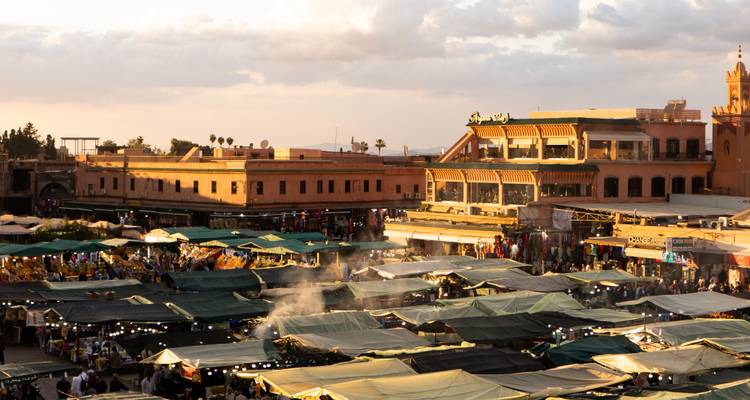 Vista elevada de la puesta de sol sobre los puestos del mercado bulliciosos y los tejadillos de la plaza principal de Marrakesh.
