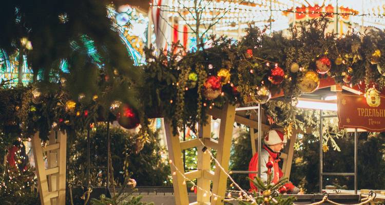 Petit kiosque de marché festif orné de guirlandes et de boules de Noël où un vendeur en costume prépare des articles.