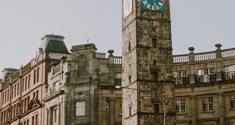Le Tolbooth Steeple historique avec son cadran d'horloge d'un bleu éclatant s'élève au-dessus des bâtiments classiques en grès dans une lumière vive.
