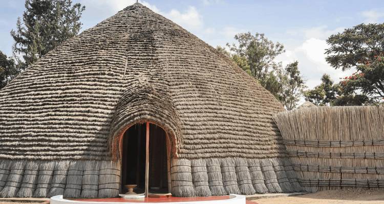 Traditionele Rwandese hut met rieten dak en een lage gewelfde deuropening binnen een historisch complex.
