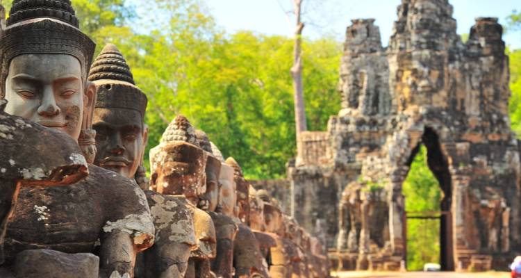 Row of weathered stone guardian statues leading to an ancient temple gate surrounded by jungle.