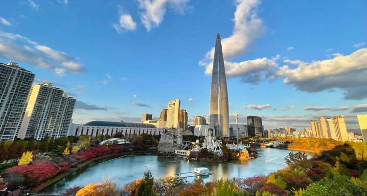 Lebendige Stadtlandschaft von Seoul mit dem aufragenden Lotte World Tower neben einem See und Herbstlaub unter kristallklarem Himmel.