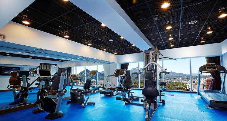 Großzügiges Hotel-Fitnesscenter mit Cardio- und Kraftmaschinen mit Blick auf große Fenster, die die Bergsilhouette rahmen.