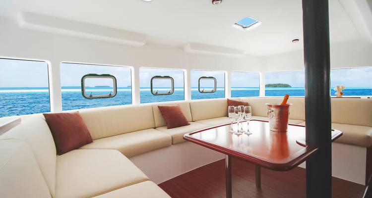 Elegante Yacht-Lounge mit cremefarbenen Sofas, Meerblick durch quadratische Fenster und Champagnergläser auf dem Tisch