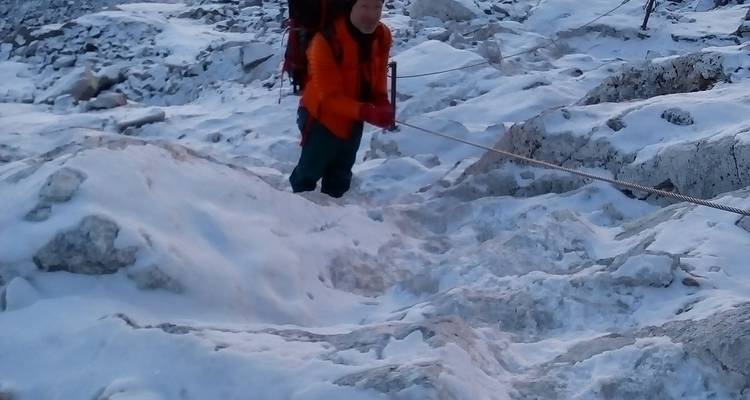 Klimmer in oranje jas klimt een ijzige helling op met behulp van een touw tussen sneeuwige rotsen.