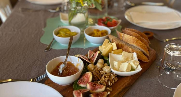 Tabla de quesos y frutas gourmet con higos, nueces, mermeladas y panes dispuestos en una mesa de comedor.