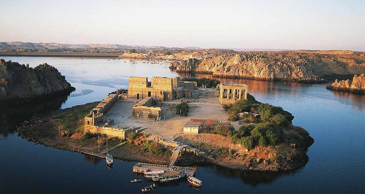 Vue aérienne du complexe du Temple de Philae sur une petite île entourée par les eaux calmes du Nil au coucher du soleil.