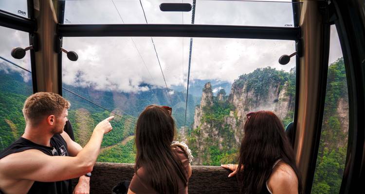 Reisende in einer gläsernen Seilbahn deuten auf die nebelverhangenen Säulenberge von Zhangjiajie.