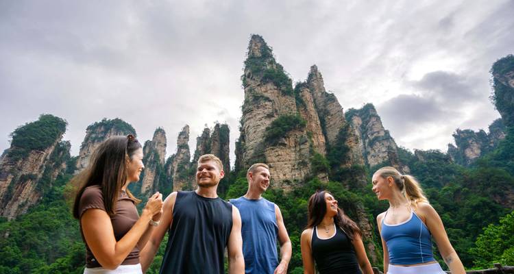 Gruppe chattet glücklich vor imposanten Karstpfeilern in Zhangjiajie unter düsterem Himmel.
