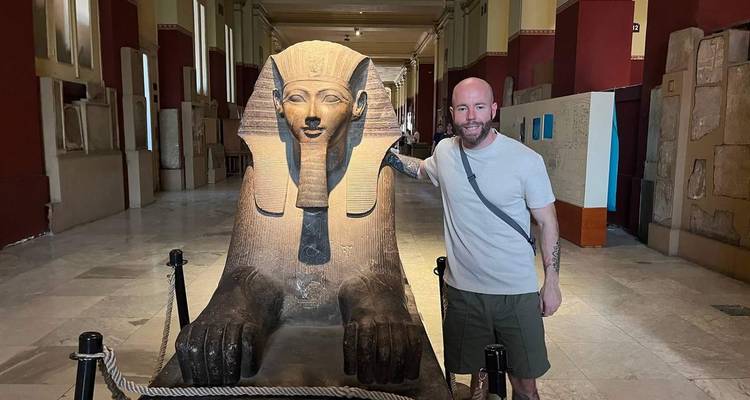 Un voyageur pose à côté d'une statue du sphinx ancien dans une galerie de musée.
