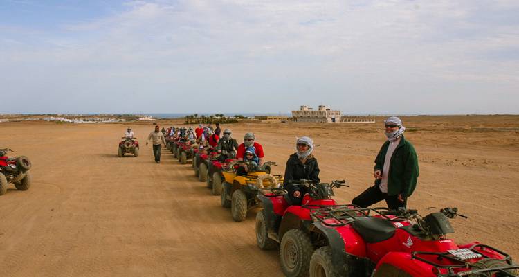 Une longue file de quads rouges avec des conducteurs casqués se prépare pour une excursion dans le désert près de la côte.