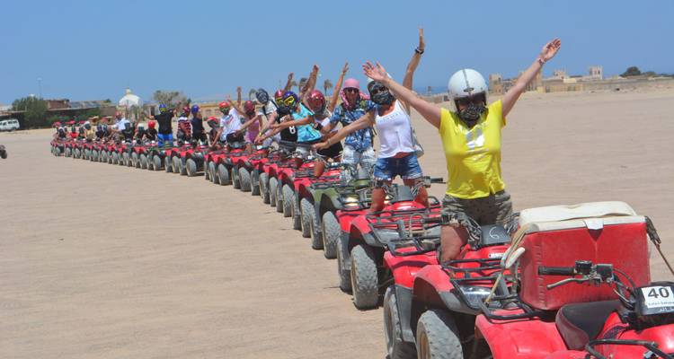 Les cavaliers sur des quads lèvent les bras dans une courbe de célébration à travers la plaine sablonneuse.