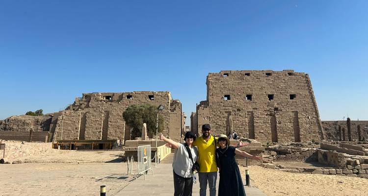 Trois amis aux bras levés se tiennent debout devant les pylônes massifs du temple de Louxor.