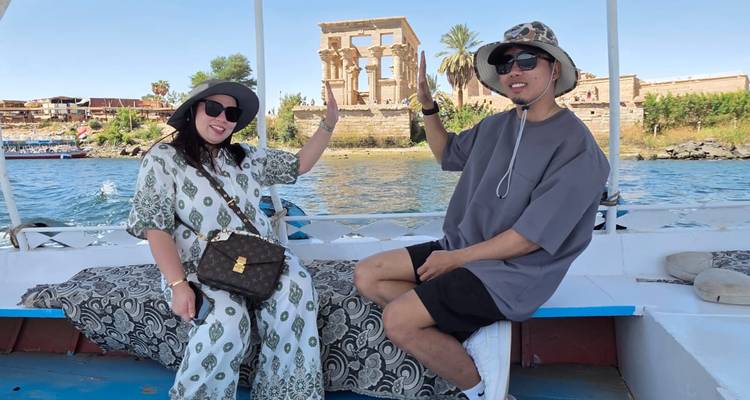 Dos turistas en una barcaza pequeña posan con las ruinas del Templo de Filae de fondo en el río Nilo.
