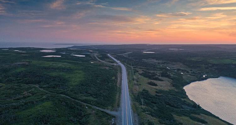 Eenzame snelweg die zich uitstrekt over glooiend groen landschap bij kleurrijke schemering.