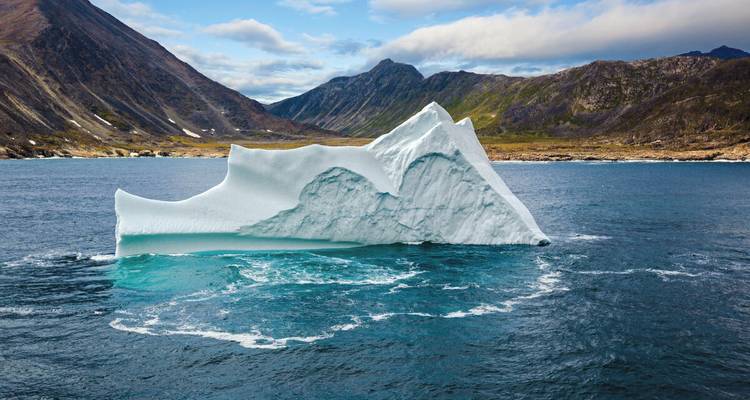 Ruwe witte ijsberg drijft in diepe fjord omgeven door steile berghellingen.