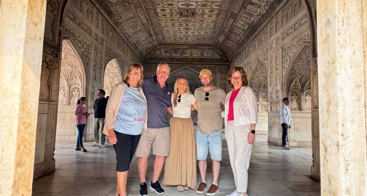 Vijf reizigers in een sierlijke marmeren hal met gedetailleerde Mughal-snijwerk die poseren voor een foto