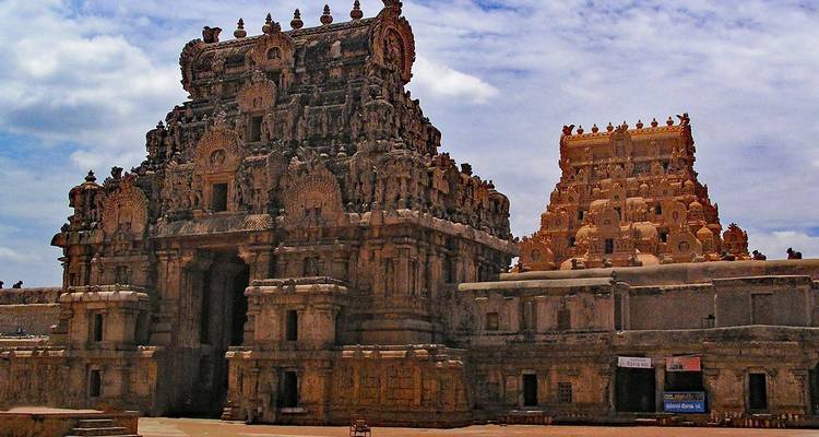 Ingewikkeld uitgehouwen stenen torens van het Brihadeeswarar Temple complex onder gedeeltelijk bewolkte lucht.