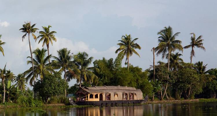 Traditionele houten woonboot drijvend op de rustige backwaters van Kerala, omgeven door palmbomen.