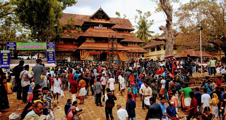 Een grote menigte verzamelt zich buiten een traditionele Keralatempel met houten architectuur en feestelijke banners.