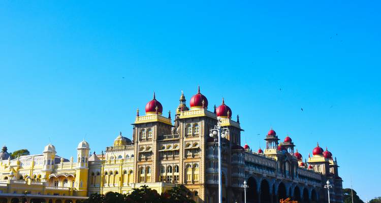 Grand Mysore Palace met rode koepels en sierlijk gevelwerk dat glinstert onder een heldere blauwe hemel.