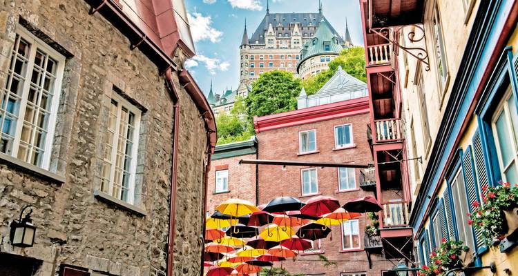 Farbenfrohe Schirme, die über einer engen Steingasse aufgespannt sind, mit dem Château Frontenac, das sich majestätisch im Hintergrund erhebt