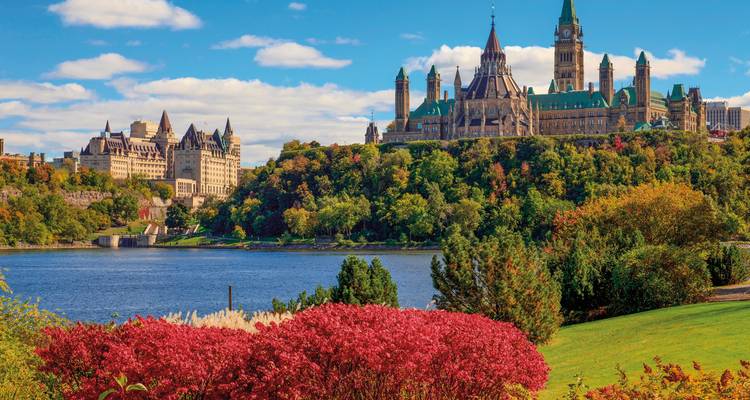 Das Parlamentshügel und das Fairmont Château Laurier erheben sich über herbstlich gefärbte Bäume entlang des Ottawa River