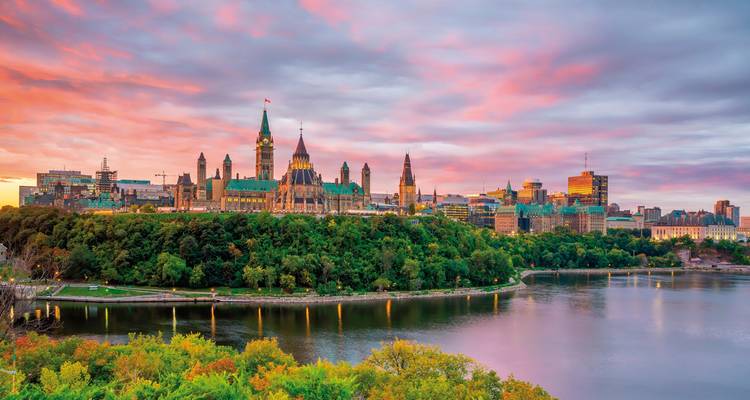 Skyline von Ottawa mit Parlamentsgebäuden unter einem dramatischen rosa Sonnenuntergangshimmel, gespiegelt im Fluss darunter
