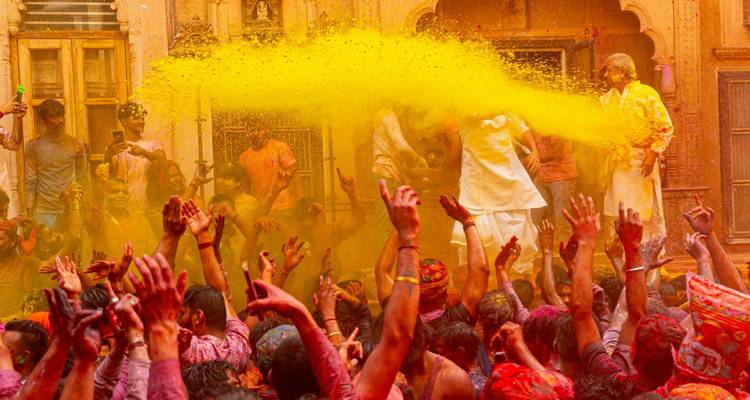 Une foule célèbre Holi à l'intérieur d'un temple alors qu'une énorme explosion de poudre jaune vif pleut sur les mains levées.