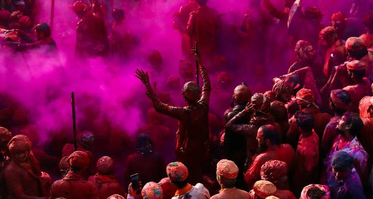 Les participants enveloppés dans des nuages de poudre magenta lèvent les bras dans une célébration joyeuse durant Holi.