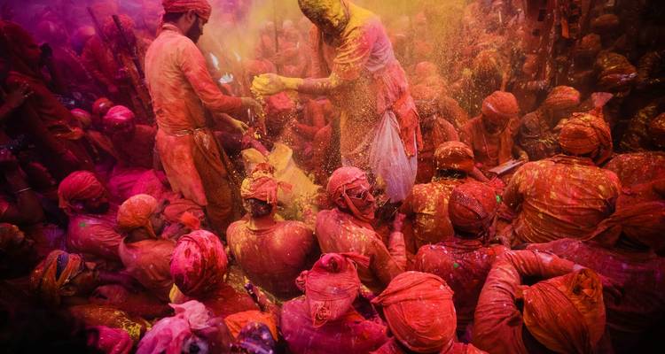 Un sol de temple bondé fourmille de personnes portant des turbans rouges s'aspergeant mutuellement de poudres colorées lors des rituels de Holi.