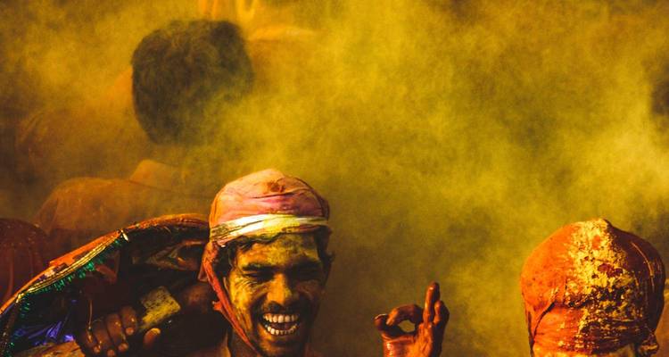 Un homme sourit au milieu d'une brume dorée de poudre colorée, les doigts formant un signe d'approbation lors des festivités de Holi.