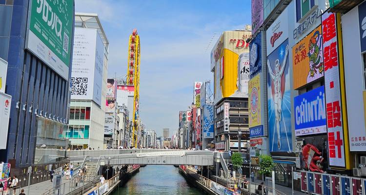 Scène animée du canal à Dotonbori à Osaka avec de hauts panneaux publicitaires et un ciel bleu dégagé