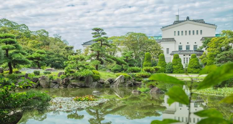 Jardin japonais serein avec pins taillés, bassin réfléchissant et un bâtiment classique blanc