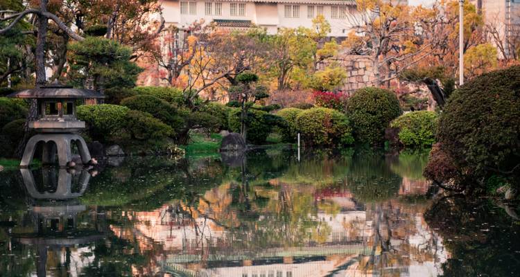 Le feuillage automnal et une lanterne de pierre se reflétant dans un étang tranquille à l'intérieur d'un jardin japonais traditionnel