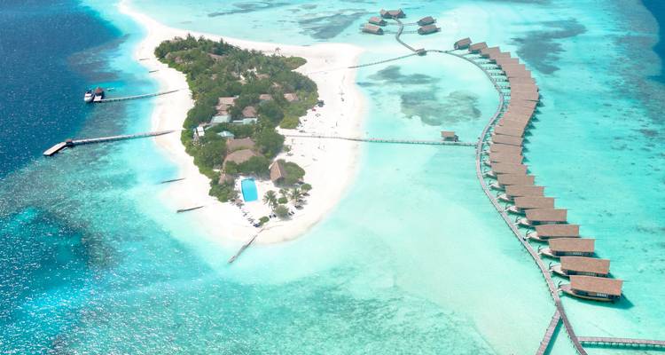 Vue aérienne d'une petite station balnéaire tropicale avec des bungalows sur pilotis entourés par un océan turquoise.