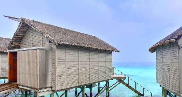 Bungalow en bois sur pilotis surplombant un lagon turquoise.