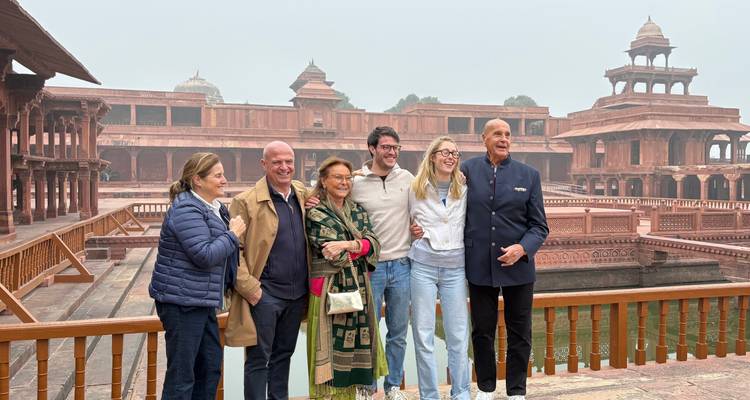 Eine Familiengruppe lächelt für ein Foto auf einem hölzernen Balkon innerhalb des Komplexes aus rotem Sandstein von Fatehpur Sikri.