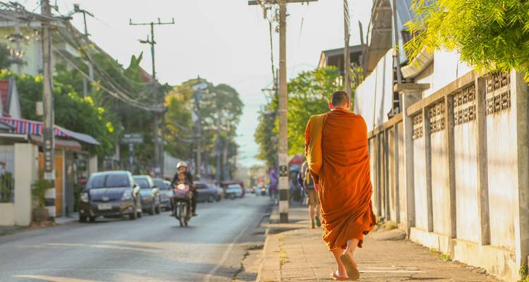 Monje descalzo en túnica naranja camina por una tranquila calle de Chiang Mai bajo la suave luz de la mañana.