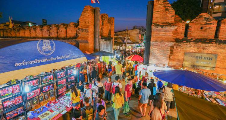 Marché nocturne bondé à la Porte Tha Phae de Chiang Mai avec des étals lumineux et des acheteurs affairés.