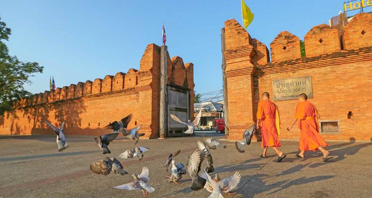 Deux moines bouddhistes passent devant la Porte Tha Phae alors que des pigeons s'envolent à la lumière du matin.