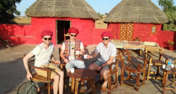 Tres viajeros con turbantes rojo brillante disfrutando de té fuera de las tradicionales chozas de adobe en el Desierto de Thar.