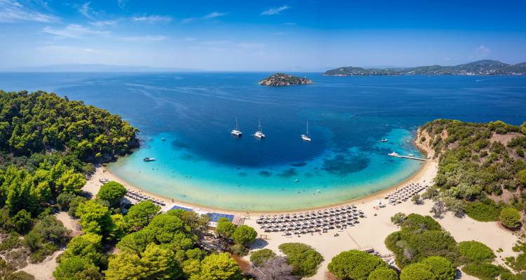 Panoramisch dronezicht van een perfect halvemanvormig strand met turquoise water, jachten en weelderige groene heuvels.