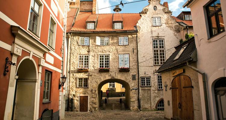 Cour pavée de charme avec une porte cintrée encadrée par la pierre historique et les bâtiments aux teintes pastel de la vieille ville de Riga.