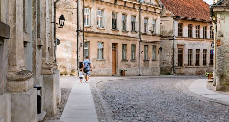 Rue historique tranquille aux façades patinées où deux personnes se promènent le long d'une courbe de pavés.