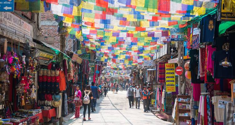 Une rue animée de Katmandou bordée de boutiques et décorée de rangées de drapeaux de prière colorés suspendus au-dessus.