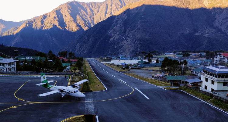 Petits avions à hélices garés sur la piste inclinée de l'aéroport de Lukla, entourés de hautes montagnes.