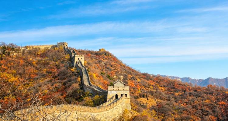 De Chinese Muur kronkelend over herfstgekleurde heuvels onder een stralend blauwe lucht.